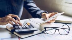 Person using calculator with papers and eyeglasses on table